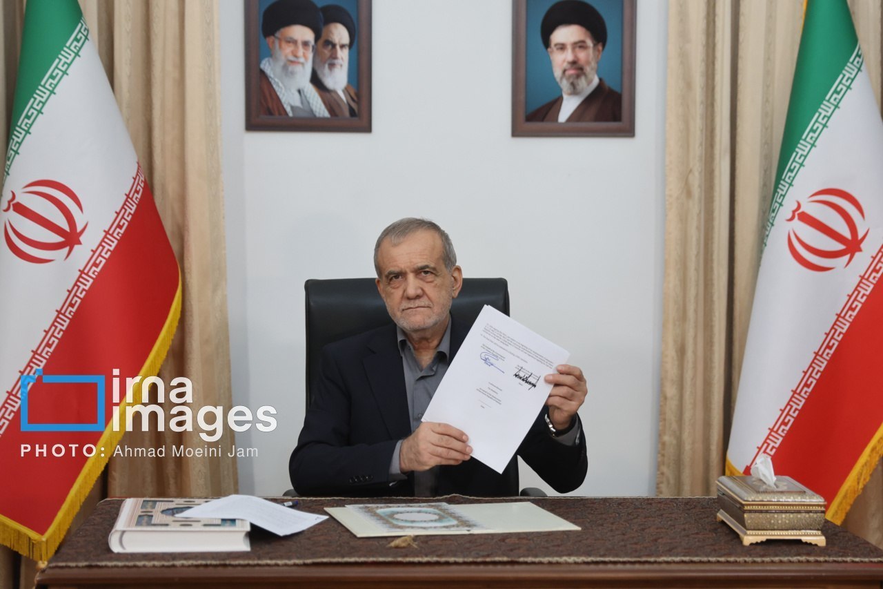 President Masoud Pezeshkian, seated at a desk between two Iranian flags, holds up the signed memorandum of understanding